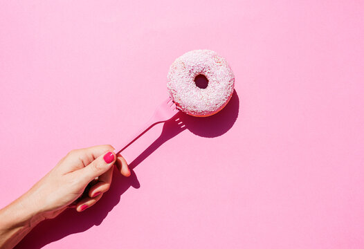 Hand of woman holding fork with sweet doughnut