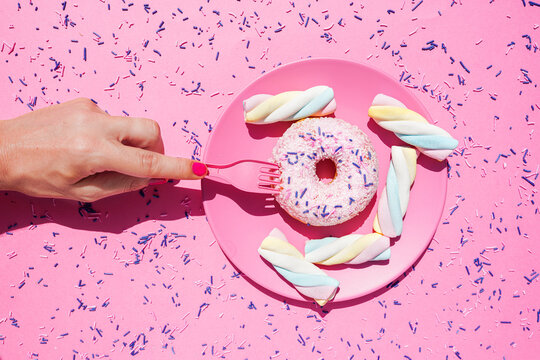 Hand of woman picking up doughnut from plate of sweets