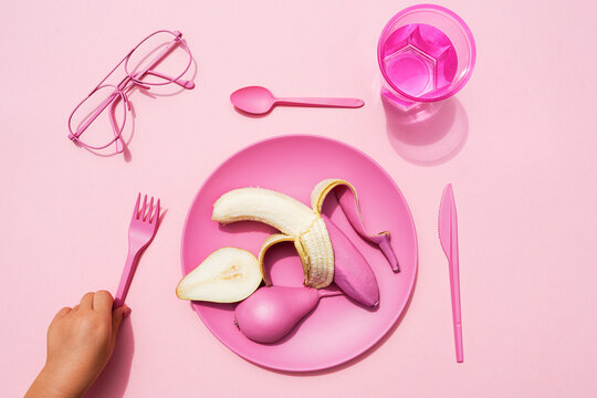 Hand of baby girl picking up fork beside plastic plate with pink-colored pear and banana