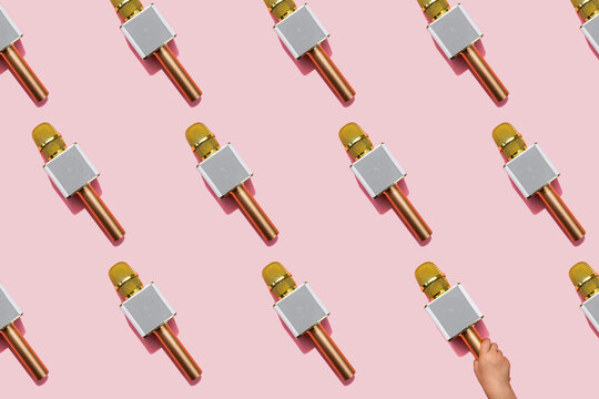 Pattern of golden microphones against pink background with hand of baby girl picking one up