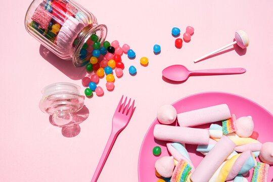 Studio shot of plastic plate filled with various sweets and candies spilling out from toppled jar