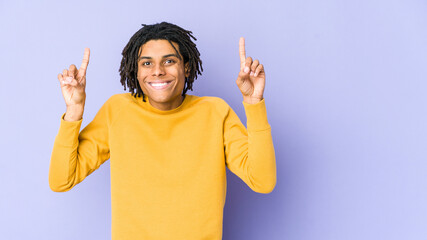 Young black man wearing rasta hairstyle indicates with both fore fingers up showing a blank space.