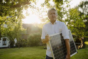 Wrinkled man holding solar panel in backyard