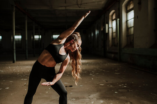 Sportswoman exercising while standing at abandoned factory