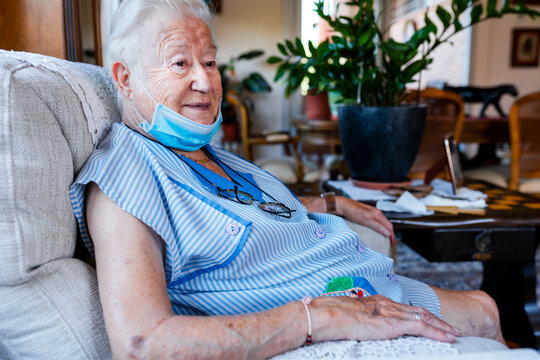Female senior with protective mask sitting in armchair at home