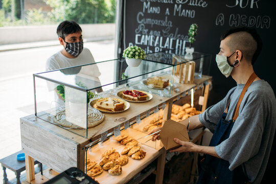 Waiter and customer with protective masks at the counter in a cafe