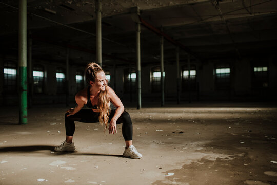 Blond woman smiling while crouching at abandoned factory