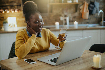 Happy black woman toasting with Champagne during video call at home.