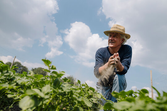 Wrinkled man looking away while mud sliding through fingers against cloudy sky