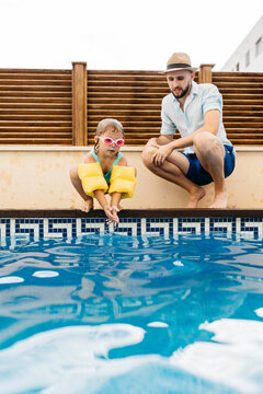Little girl jumping into water, her uncle at poolside