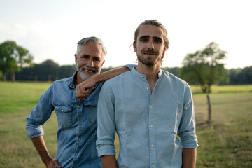 Portrait of happy father with adult son on a meadow in the countryside