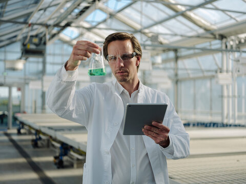 Scientist with tablet examining liquid in a greenhouse