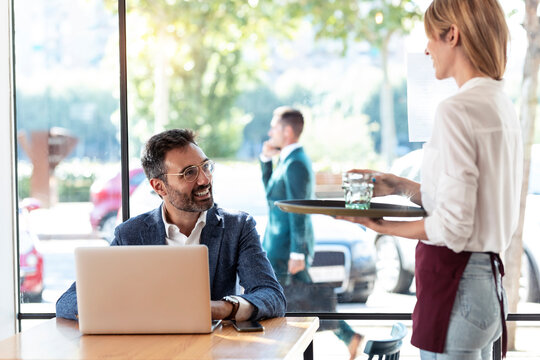 Smiling businessman looking at waitress holding glass of water in restaurant
