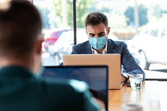 Businessman wearing protective face mask while using laptop in cafe during coronavirus outbreak