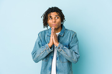 Young black man wearing a jeans jacket praying, showing devotion, religious person looking for...