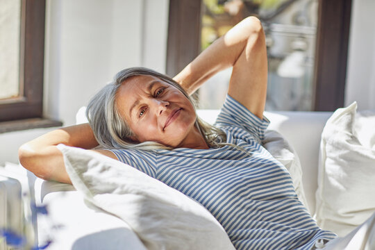 Smiling woman relaxing with hands behind hand on sofa in living room