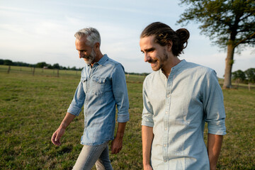 Happy father and adult son walking on a meadow in the countryside