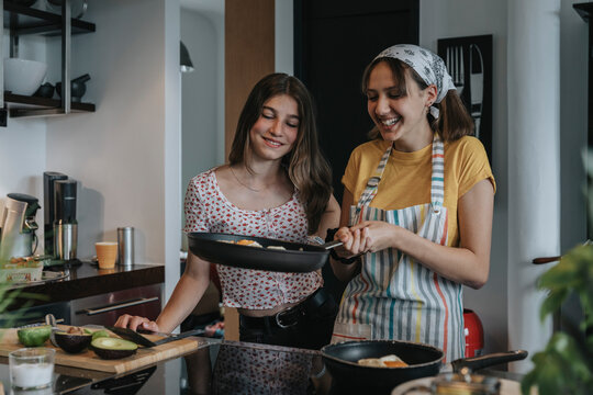 Girlfriends preparing healthy lunch together, frying eggs in kitchen