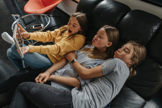 Three girlfriends sitting on couch. takinga selfie with digital tablet