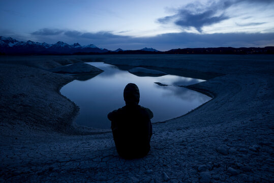 Germany, Bavaria, Silhouette of hooded man admiring Forggensee lake at dusk