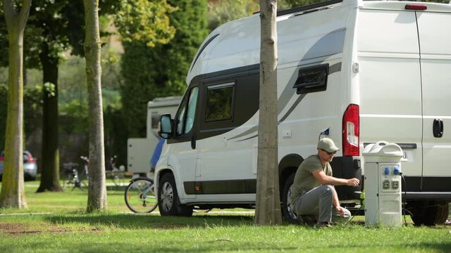 Caucasian Men Connecting Electricity Plug to His Modern RV Park Hookup Tower. Camping Time Theme.