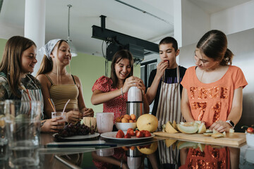 Group of teenagers standing in kitchen, preparing smoothies with a blender