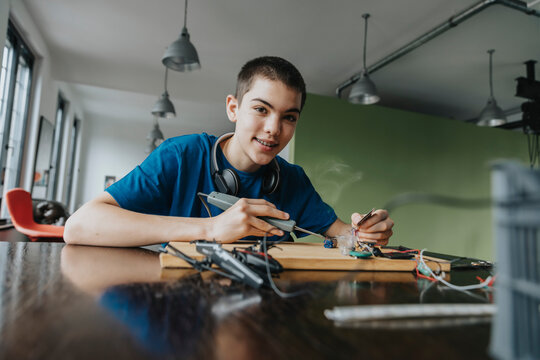 Boy sitting at home using soldering iron