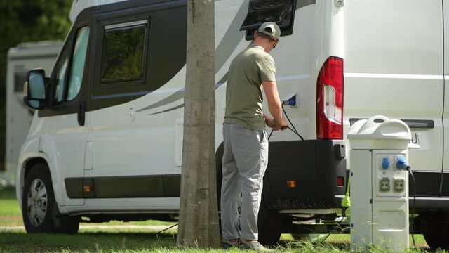 Caucasian Vacationer in His 40s Connecting Electricity Plug to RV Park Hookup. Motorhome Features.