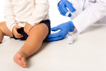 Cropped view of pediatrician holding syringe near vaccine and toddler boy isolated on white