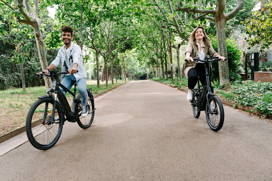 Happy young couple riding electric bicycles on road amidst trees