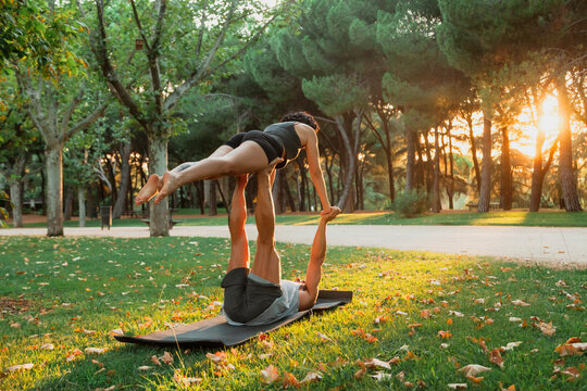 Couple practicing acroyoga in public park during sunset