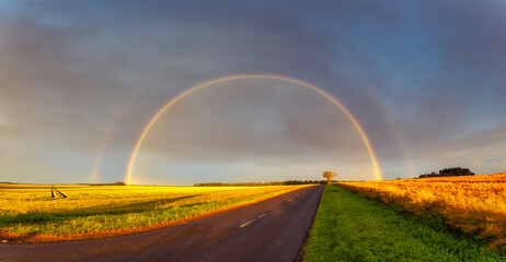 Double rainbow arching over empty countryside highway