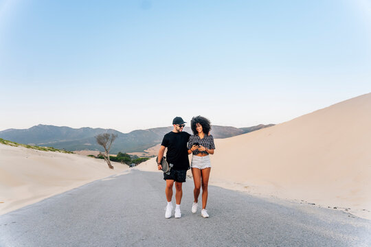Young couple walking on road by sand dune against clear blue sky