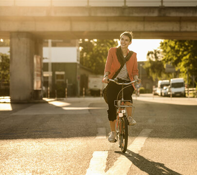 Smiling woman riding bicycle on street in city during sunny day - Powered by Adobe