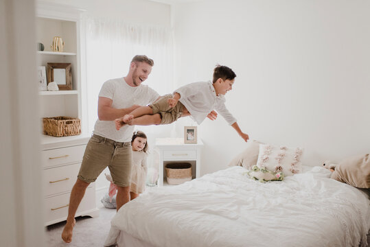Playful father throwing son over bed while daughter standing in bedroom