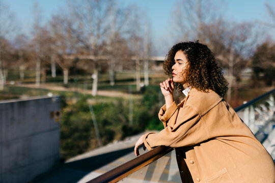 Thoughtful woman leaning on railing while looking away during sunny day