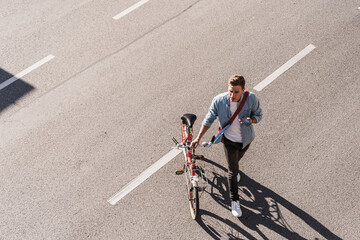 Young man crossing street with bicycle in city