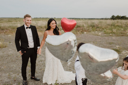 Parents and children wearing wedding dress with heart shape balloons in field against sky