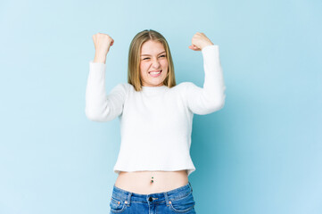 Young blonde woman isolated on blue background raising fist after a victory, winner concept.