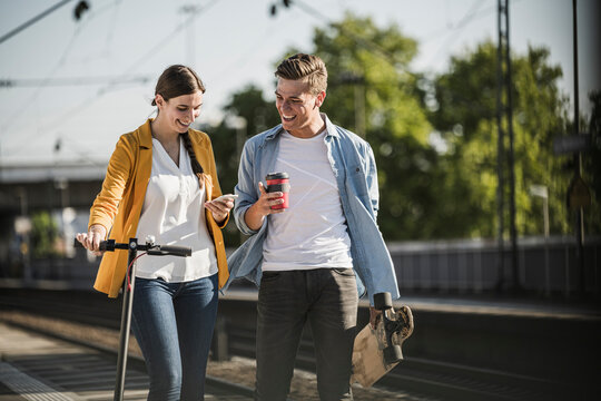 Young woman showing smart phone to male friend while walking at railroad station