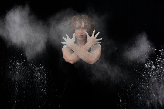 Woman throwing white dust besides herself while standing against black background