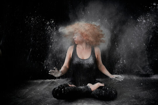 Woman tossing hair covered in white dust while sitting against black background