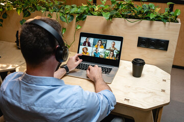 Male entrepreneur on video call with colleagues through laptop while sitting at desk in creative office