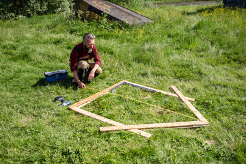 Carpenter crouching while measuring planks for playhouse on grass
