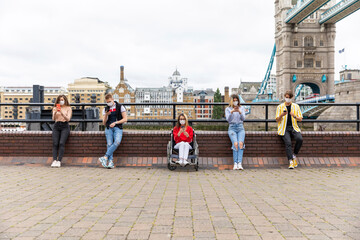 Friends maintaining safe distance and using mobile phones with Tower Bridge in background, London, UK