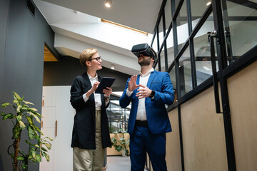 Businesswoman analyzing colleague using virtual simulation headset in creative office corridor
