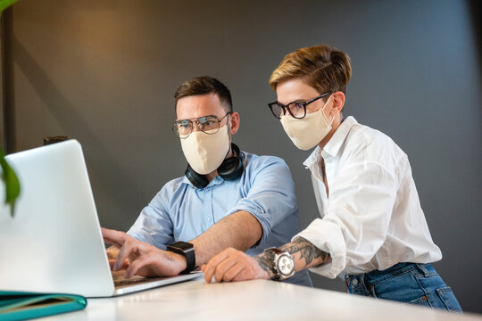 Male and female colleagues planning strategy while discussing over laptop at desk in office during pandemic
