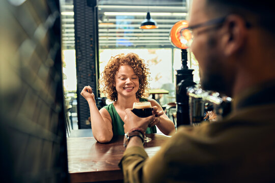 Barkeeper handing over glass of beer to woman in a pub