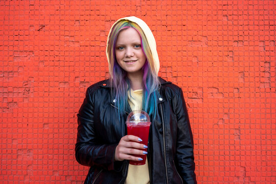 Portrait of young woman with dyed hair with takeaway drink in front of red wall