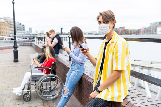 Young man keeping safe distance with friends while using mobile phones in city